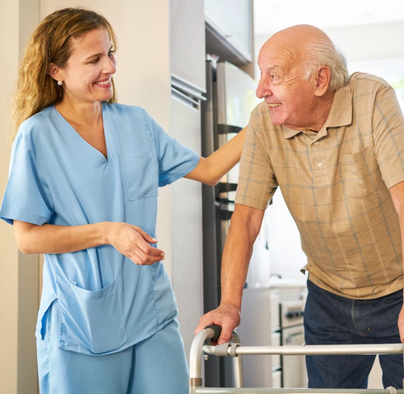 Caregiver providing companionship care and support to an elderly man using a walker at home