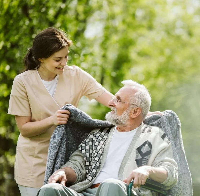 Caregiver supporting an elderly man outdoors, representing the benefits of long-term care support for family caregivers