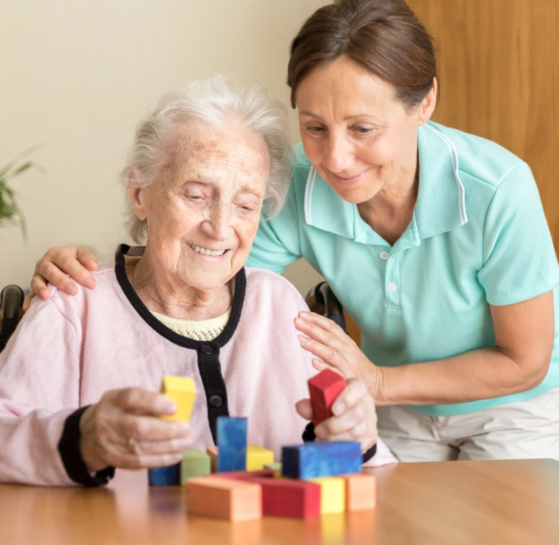 Caregiver assisting an elderly woman with dementia during a cognitive activity using colorful blocks