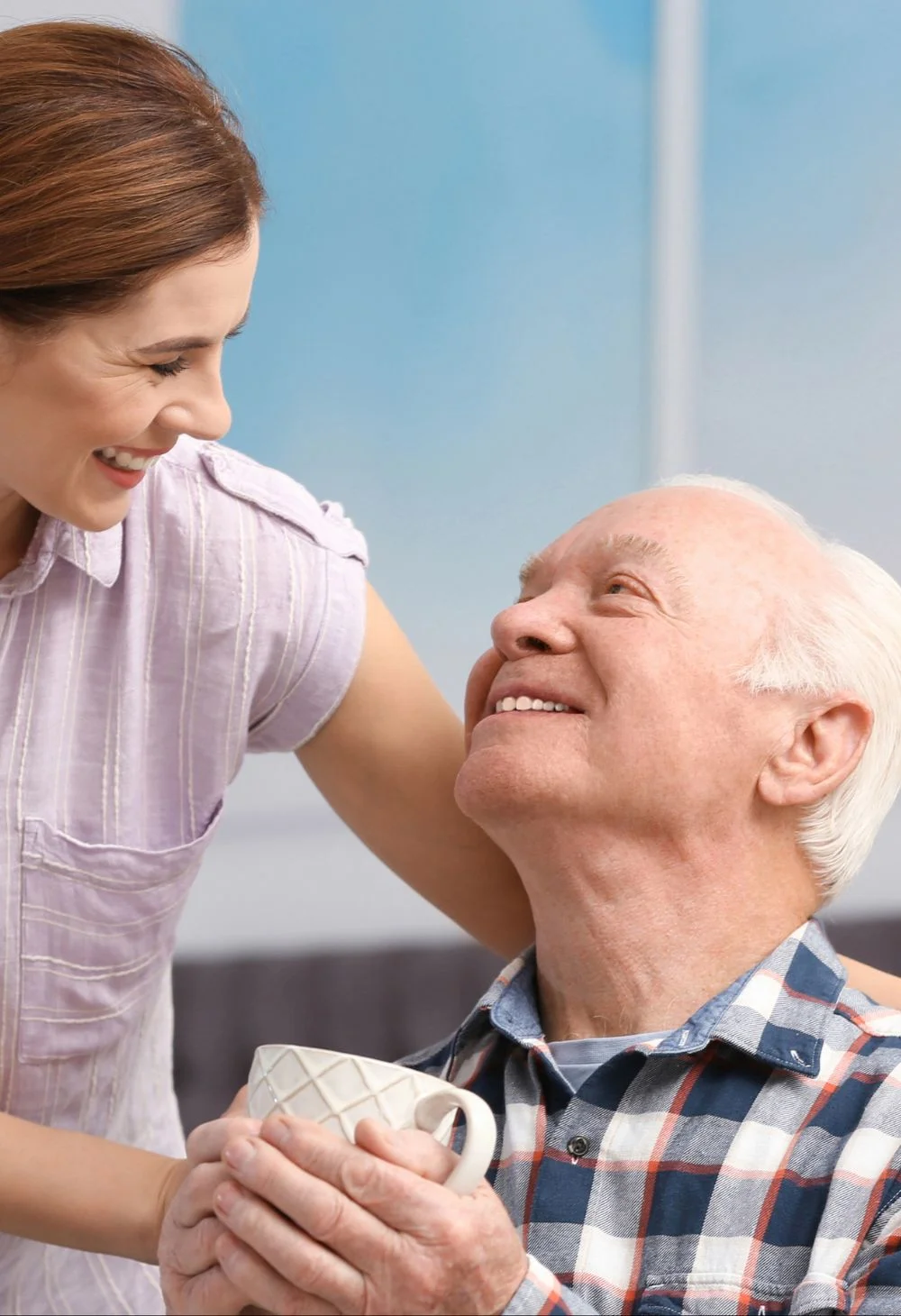 Caregiver smiling warmly at an elderly man holding a cup, representing compassionate senior care for North Las Vegas residents