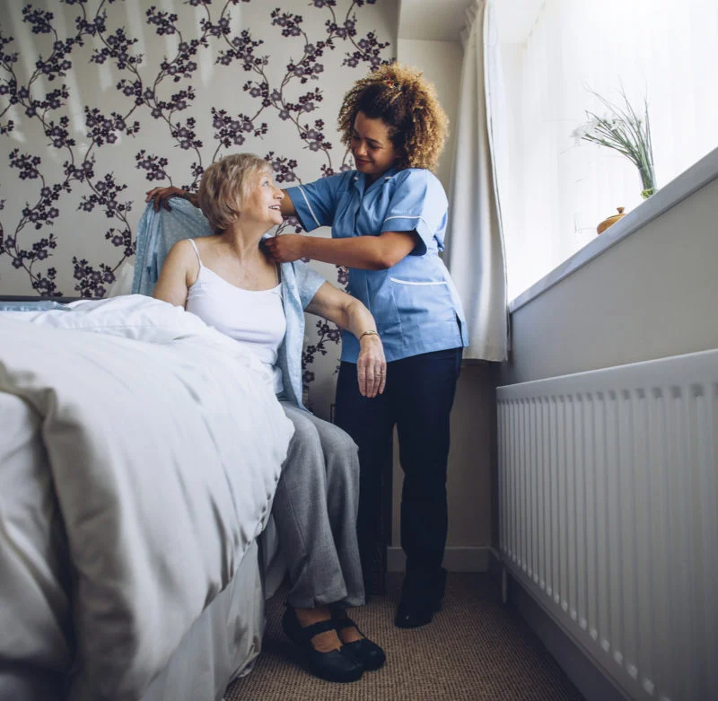 Caregiver helping a senior woman get dressed in a bedroom, representing dependable 24-hour live-in care