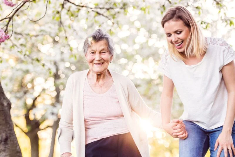 Caregiver assisting a smiling elderly woman outdoors, representing a trusted home care provider in Laughlin Nevada