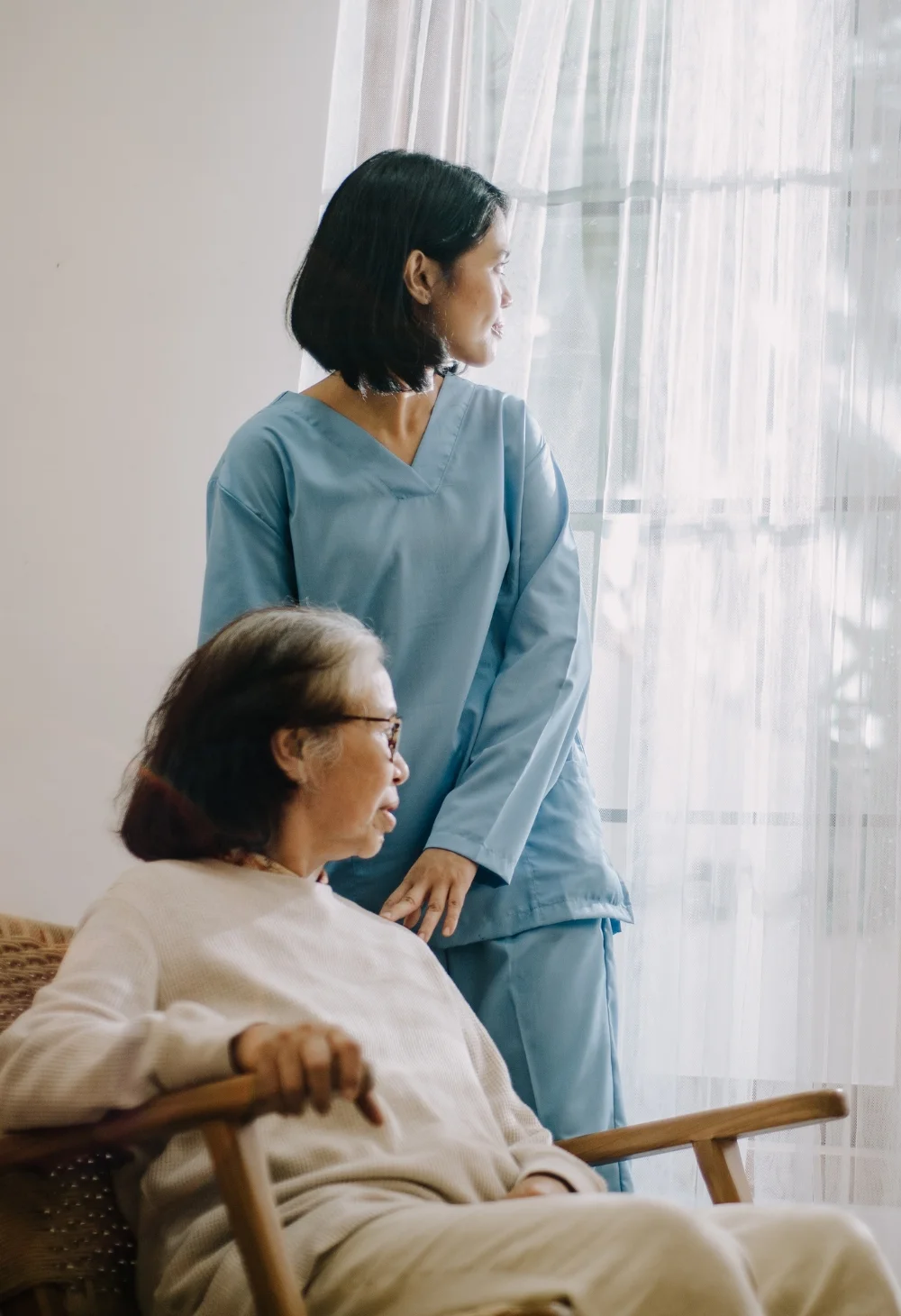 Caregiver standing beside an elderly woman near a bright window, representing compassionate senior care for Paradise residents
