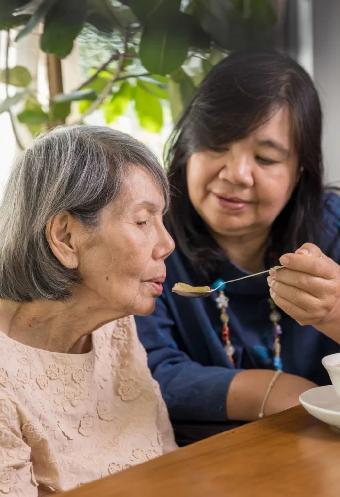 Caregiver gently assisting an elderly woman with eating as part of compassionate in-home care services