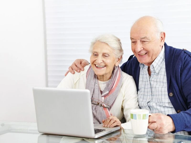 Elderly couple smiling while using a laptop together, representing digital support and connection