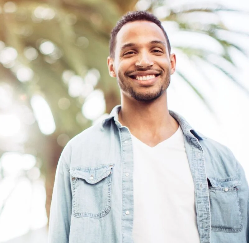 Smiling young man standing outdoors with sunlight and palm trees in the background
