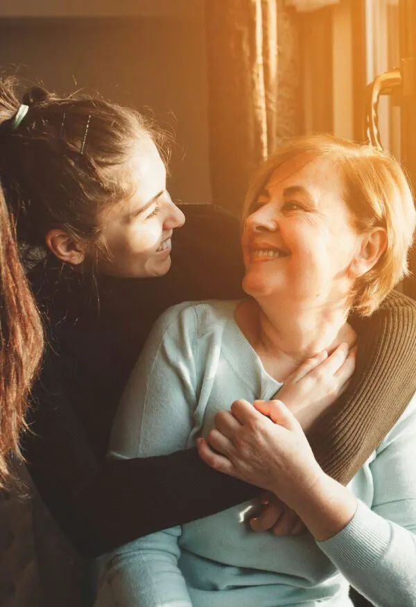 Young woman embracing and supporting an older woman at home – representing the mission and values of My Essential Care