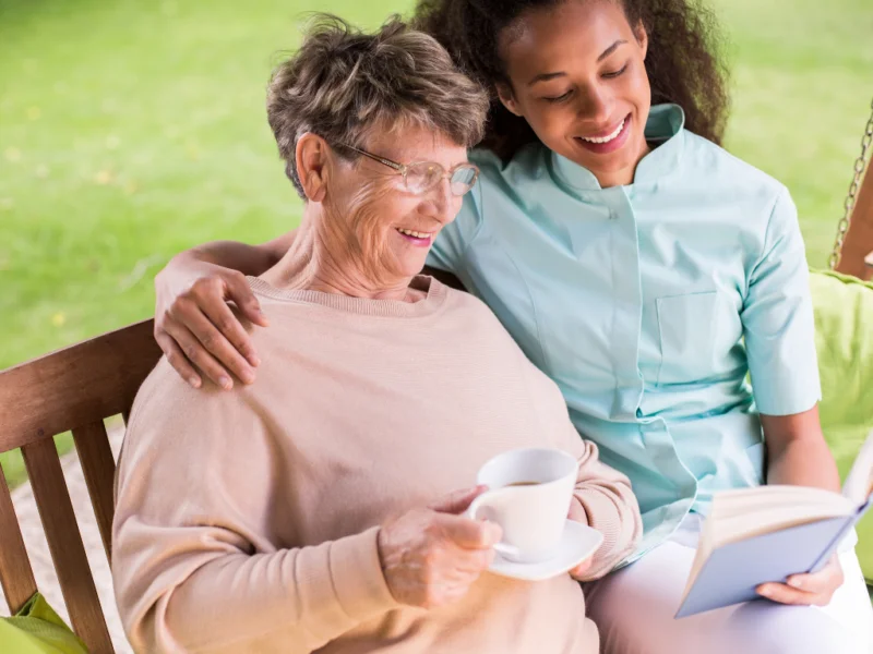 Caregiver reading with an elderly woman while providing warm and supportive personal care